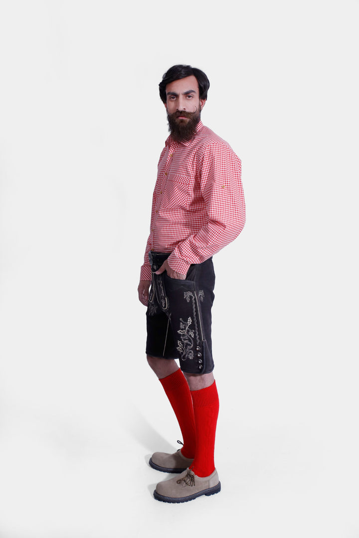 Side profile of a man in Steuben Lederhosen, emphasizing the brown leather shorts' design, embroidery, and fit, paired with a red checkered shirt, red socks, and beige-colored shoes.