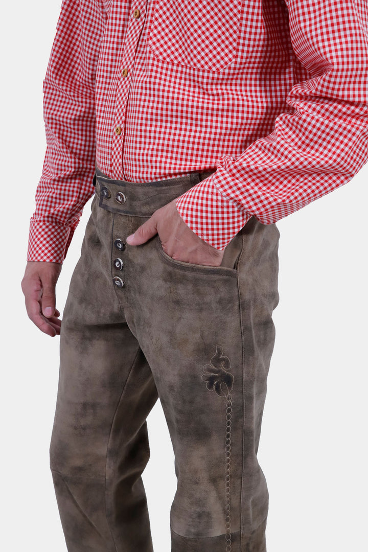 Side view of a person standing with hands in pockets, wearing Wachau Valley Lederhosen Long Pant with intricate embroidery and a red and white checkered shirt.