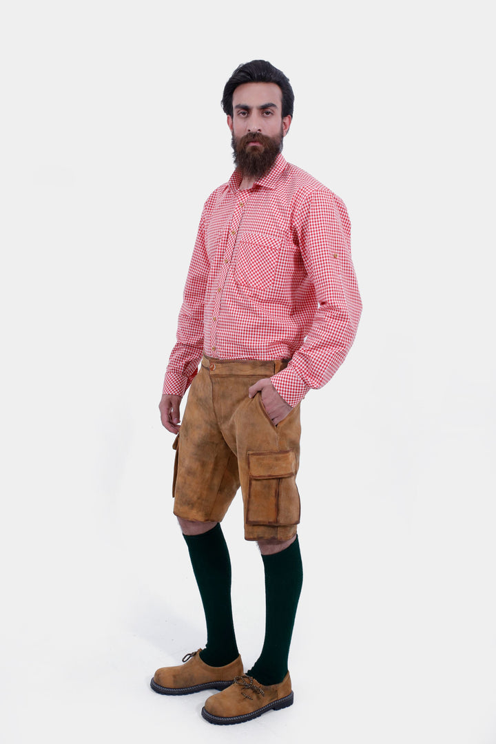 Full-body view of a man wearing Wagner Cargo Lederhosen paired with a red checkered shirt, knee-high green socks, and brown shoes, demonstrating traditional Bavarian attire.