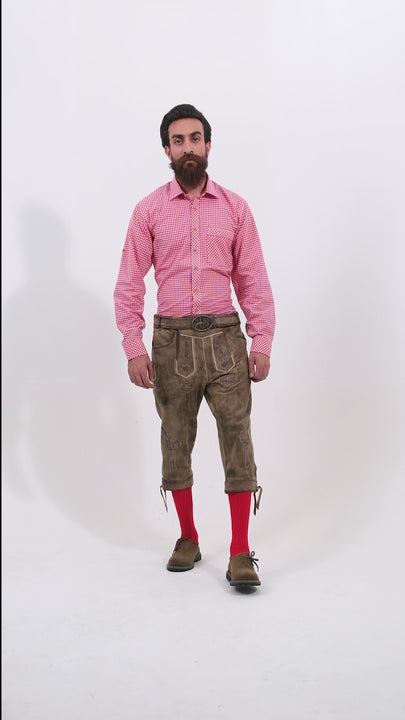 Male model wearing a red checkered shirt and Milwaukee Bundhosen, featuring intricate embroidery on the front, a decorative belt buckle, and mid-length. The model's hands are by his sides, and he is wearing brown shoes with socks, showcasing the traditional bundhosen in a rotating video to display all angles.