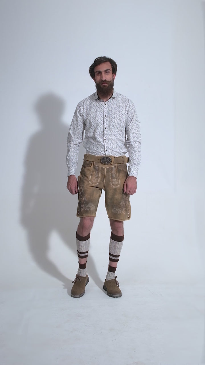 Video showing a 360-degree view of the Mozart Lederhosen worn by a man in a white patterned shirt and beige shoes, highlighting the detailed craftsmanship, embroidery, and features of the traditional Bavarian leather shorts.