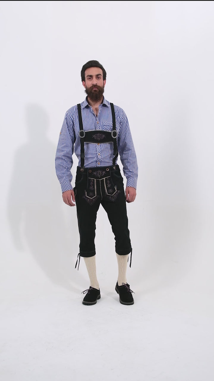 Male model wearing a blue checkered shirt and Marx Bundhosen, featuring intricate embroidery on the front, a decorative belt buckle, and mid-length. The model's hands are by his sides, and he is wearing black shoes with socks, showcasing the traditional bundhosen in a rotating video to display all angles.