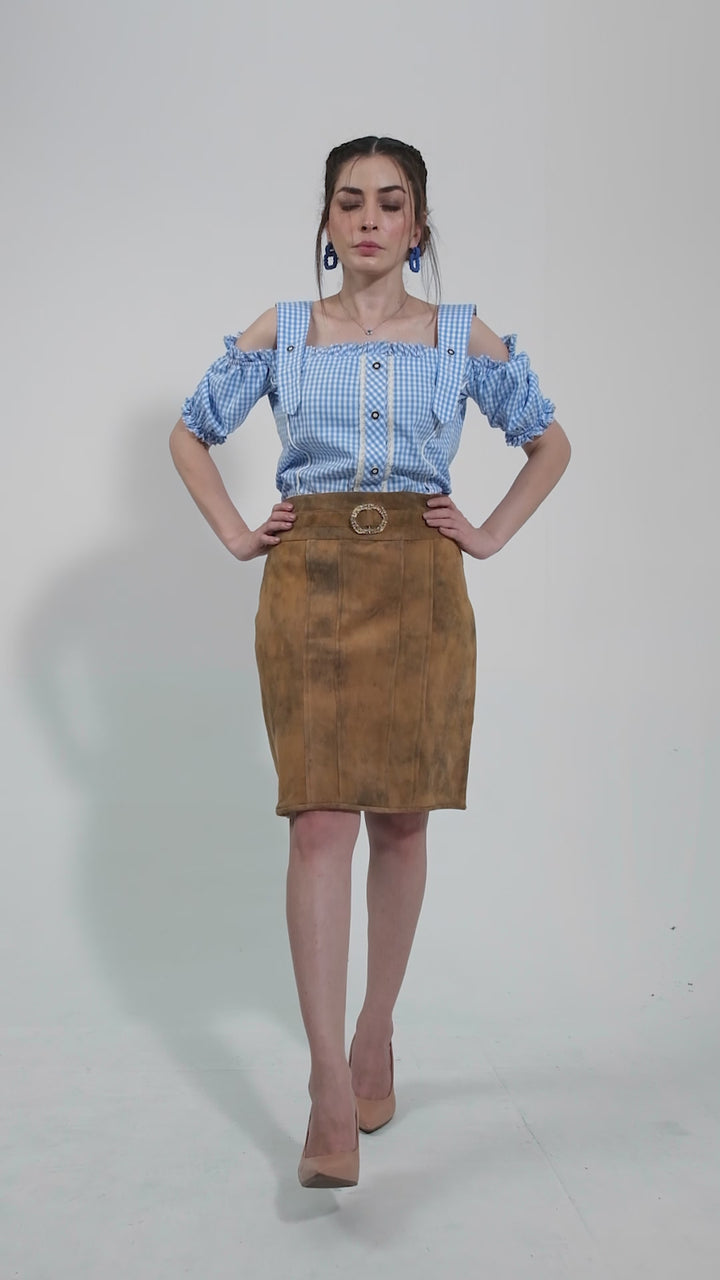 video featuring a model showcasing a traditional leather skirt paired with a blue and white checkered blouse. The model poses in different angles, highlighting the skirt's intricate details and rustic texture. The video aims to emphasize the authentic craftsmanship and stylish versatility of the Clara Lederhosen Skirt, perfect for cultural events and fashionable outings