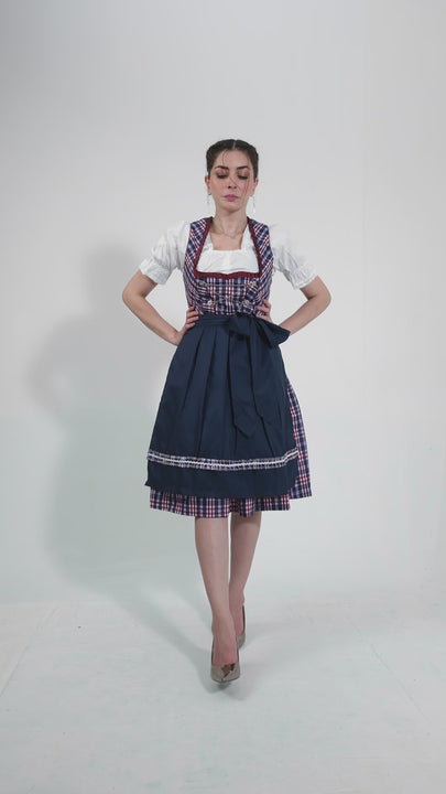 Video showcasing the Dirndl Hilker, featuring a woman elegantly modeling the outfit. She highlights the hilker bodice with plaid details, the full navy skirt, and the neatly tied apron, demonstrating the dirndl's grace and versatility for various festive occasions against a neutral backdrop.