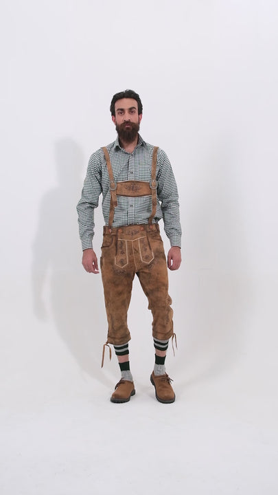 Male model wearing a checkered shirt and Hesse Bundhosen, featuring intricate embroidery on the front, a decorative belt buckle, and mid-length. The model's hands are by his sides, and he is wearing brown shoes with socks, showcasing the traditional bundhosen in a rotating video to display all angles.